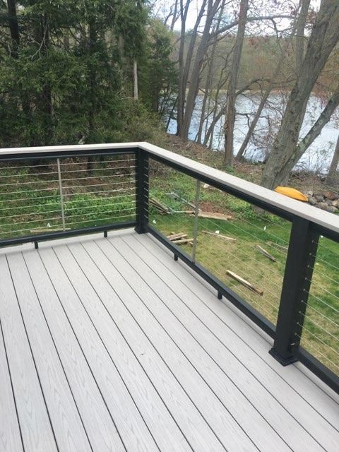 Composite deck with black railing and wire infill, overlooking a grassy yard and water.