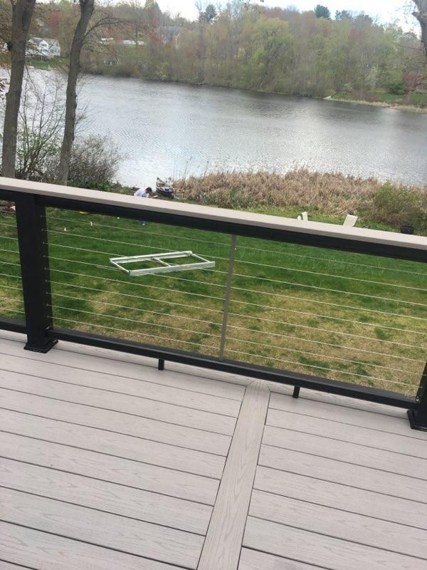 Deck with black railing, glass panels, overlooking a lake.