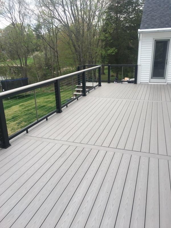 Composite deck with black railing and cable infill, next to a house with a glass door.