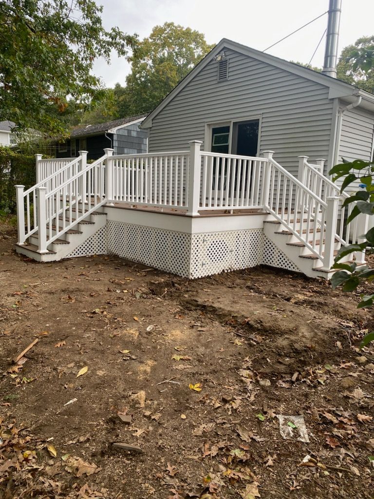 White deck with stairs, lattice skirting, attached to a gray house, set in a yard.