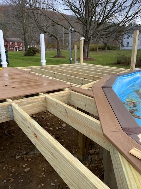 Deck under construction next to a pool. Wooden frame with some composite decking installed. Outdoors, daytime.