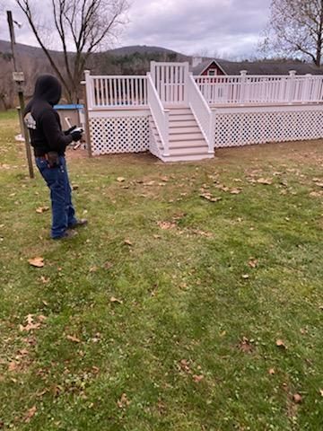 Person in a black hoodie operating a drone, near a white deck with stairs on a grassy lawn.