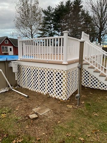 White deck with lattice skirting, stairs, and a pool in the background. Brown yard and cloudy sky.