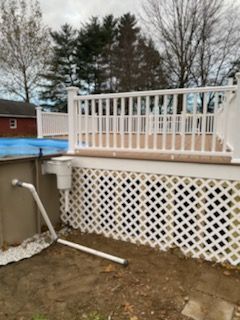 White deck with latticework skirting beside a pool with visible plumbing.