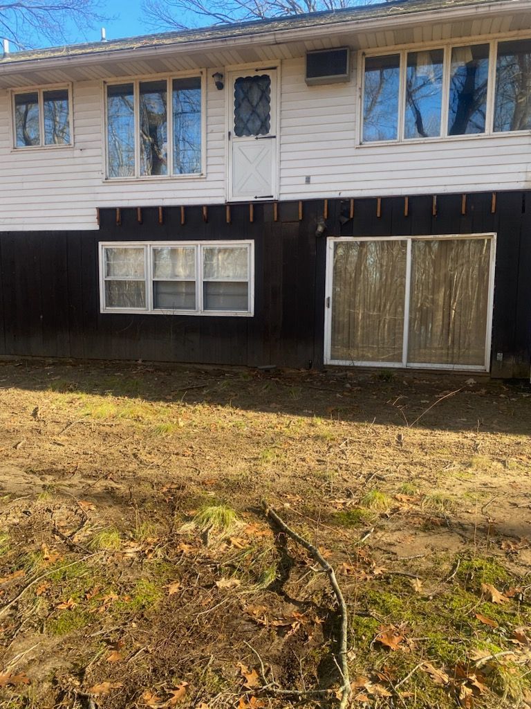 Back of a two-story house with white siding on top and brown siding below; dry, brown yard in front.