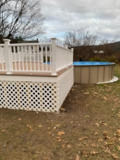 White deck with lattice skirting next to an above-ground pool on a grassy lawn.