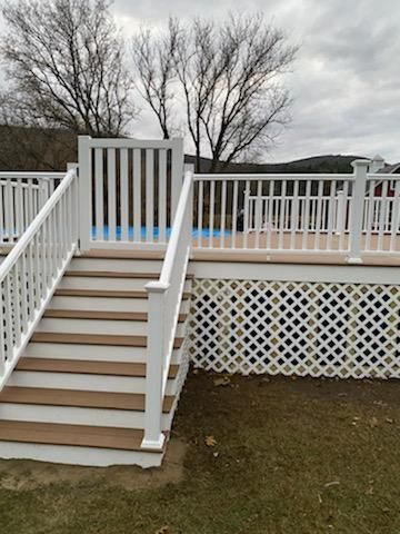 White deck with stairs, gate, and lattice, leading to a pool area. Brown steps, white railing, cloudy sky.