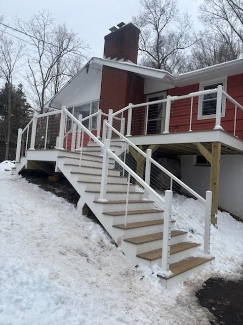 A red house with a white deck and stairs leading down a snow-covered hill.