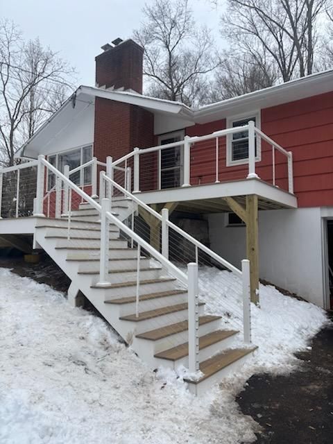 Exterior of a red house with a deck and stairs; white railings and steps with snow on the ground.