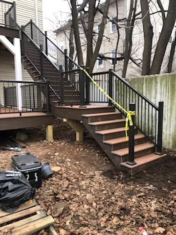 Exterior staircase with brown composite steps and black railings, under construction.