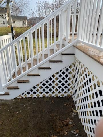 White deck stairs with lattice sides, brown treads, white railing, and a view of houses in the background.