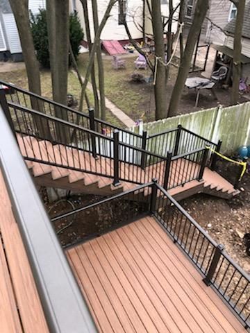Elevated composite deck and stairs with black railing and brown boards, overlooking a yard.