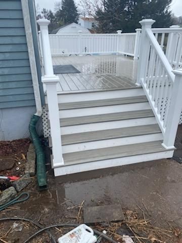 White railing and steps leading up to a deck with gray composite decking; a green downspout is visible.