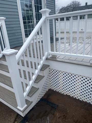 White deck with stairs, railing, and lattice skirting, against a gray house.