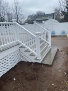 White deck and stairs with railing leading to a backyard; overcast sky.