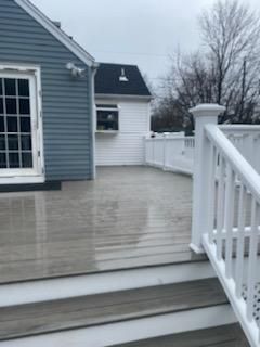 Wooden deck with white railing, steps, and a blue house in the background.