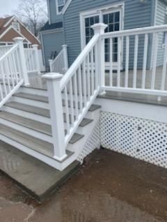 Blue house with white deck, stairs, and railing. Gray steps and lattice. Wet ground.