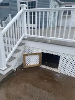 White deck with stairs, lattice skirting, and an access door over a concrete patio.