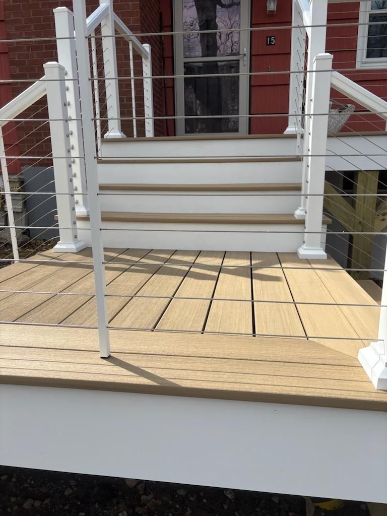 Tan deck with white railing and steps leading to a red door.