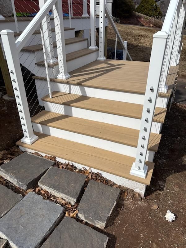 Outdoor staircase with composite decking and white railing, leading to a deck. Stone pavers are at the base.