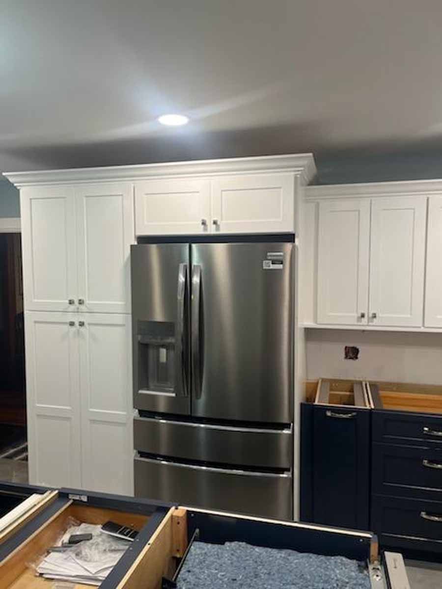 White kitchen cabinets frame a stainless steel refrigerator. Black cabinets are partially visible.