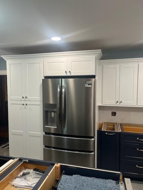 White kitchen cabinets surround a stainless steel refrigerator. A small, dark blue cabinet with drawers is visible.