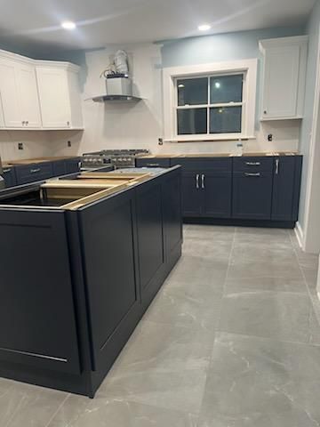 Newly renovated kitchen with dark blue cabinets, white upper cabinets, and gray tile flooring.