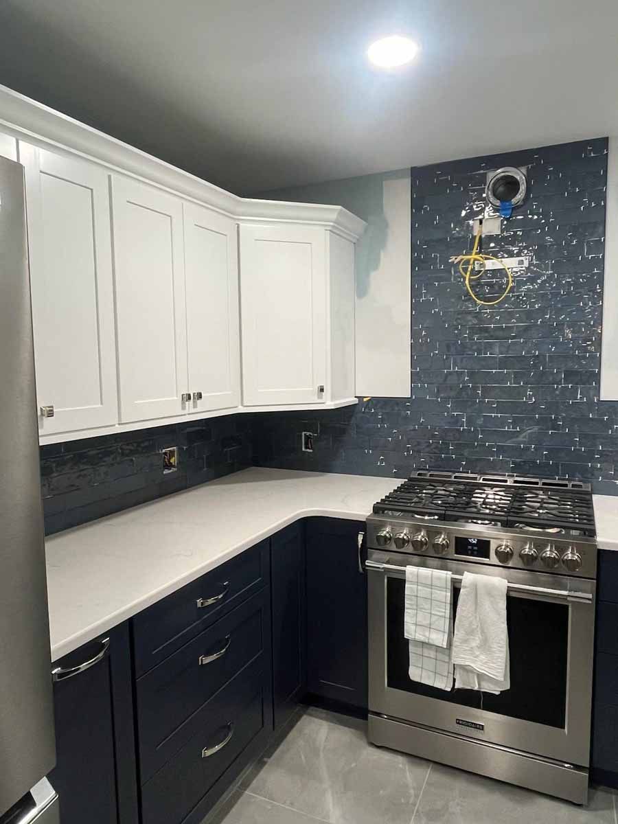 Kitchen remodel with blue and white cabinets, stainless steel range, white countertops, and blue tile backsplash.
