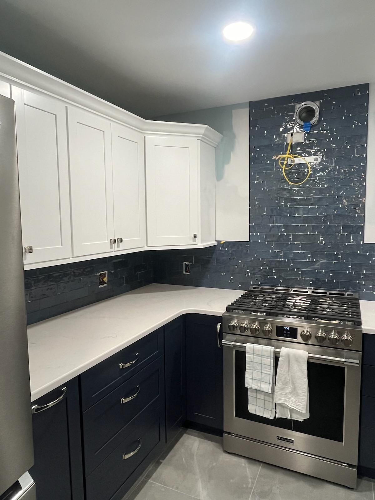 Navy and white kitchen with stainless steel oven, white countertops, and blue tile backsplash.