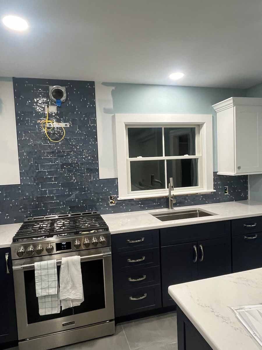Kitchen renovation with navy blue cabinets, mosaic backsplash, stainless steel range, and white countertop.