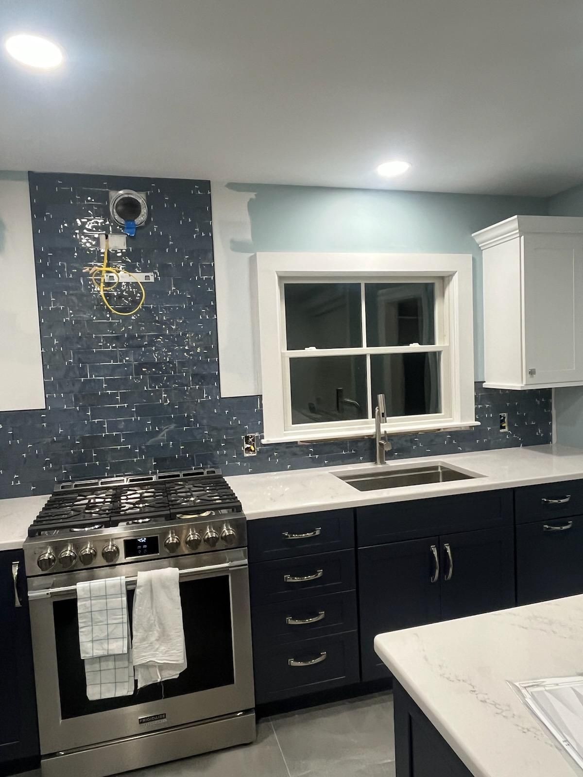Kitchen remodel in progress: blue cabinets, dark blue tile backsplash, stainless steel stove, and white countertop.