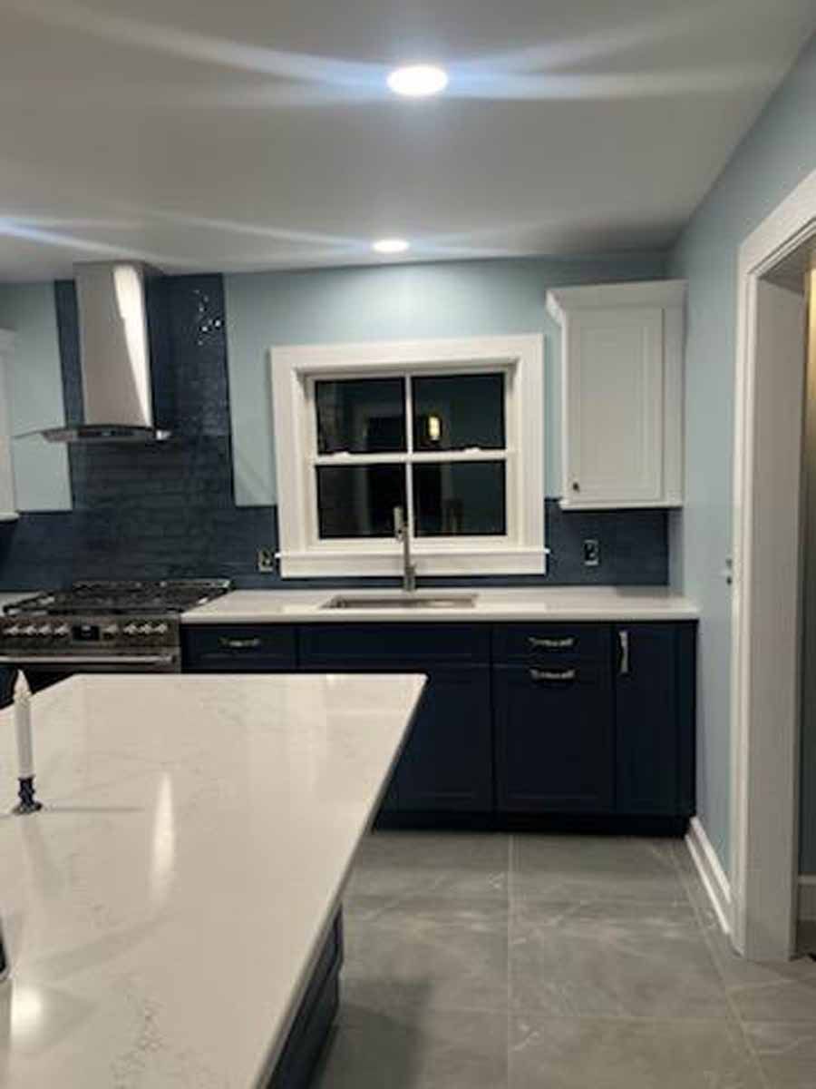 Modern kitchen with navy blue and white cabinets, white countertops, and blue tiled backsplash.