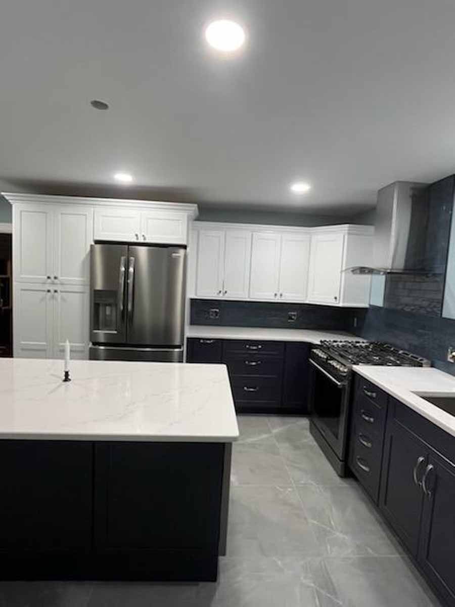 Modern kitchen with white upper cabinets and navy blue lower cabinets, stainless steel appliances, and a large island.