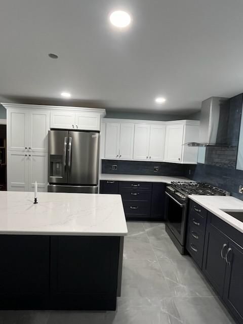 Modern kitchen with white upper cabinets and navy lower cabinets. Stainless steel appliances and a white countertop island.