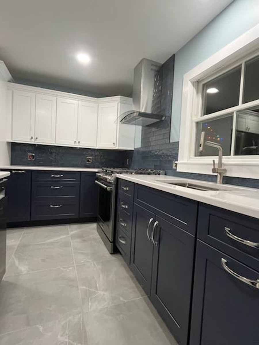 Modern kitchen with blue and white cabinets, stainless steel appliances, and gray tile flooring.