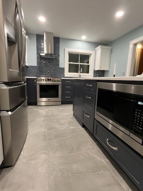 Modern kitchen with stainless steel appliances, blue cabinets, and gray tile flooring.