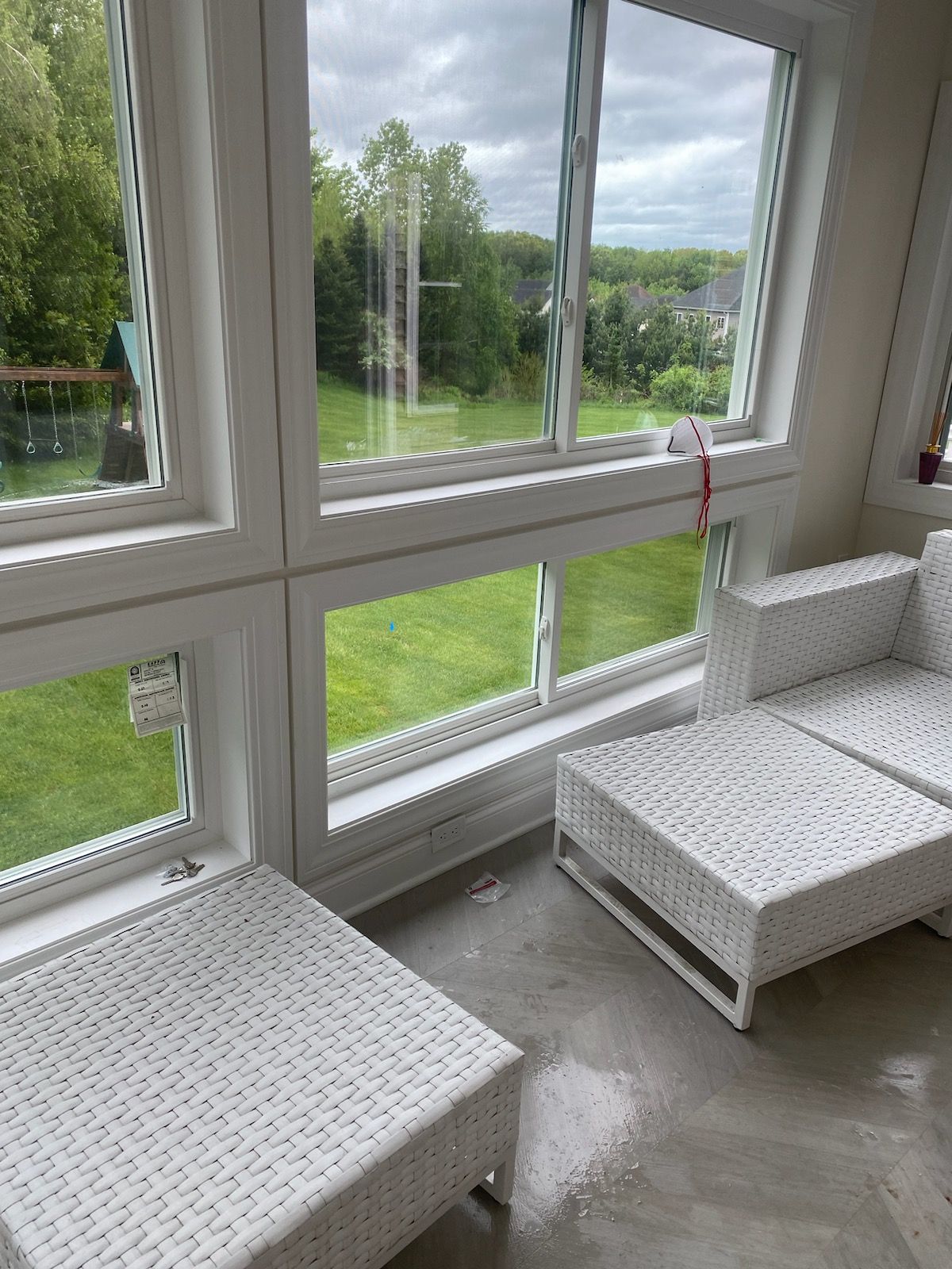 White wicker furniture near large windows overlooking a green lawn under a cloudy sky.