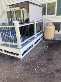 A backyard deck with a gazebo, white railing, and gray accents. A large propane tank sits nearby.