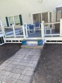A brick pathway leads to a deck with blue chairs, potted plants, and white railing.