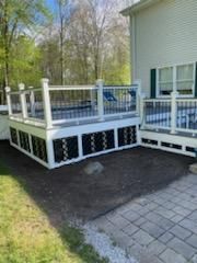 White deck with black accents next to a house with pavers and grass.