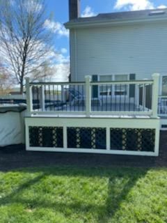 White deck with black lattice panels, black railings, and white posts. Green grass in foreground.