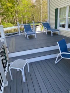 Deck with gray composite decking, blue lounge chairs, white railing, and a small table.