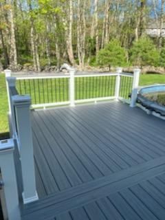 Gray composite deck with white railing, black spindles, overlooking a wooded area.