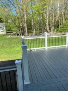 Gray deck with white railing, black spindles, and trees in background.