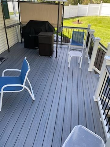 Gray composite deck with blue chairs, a grill, and black railing.