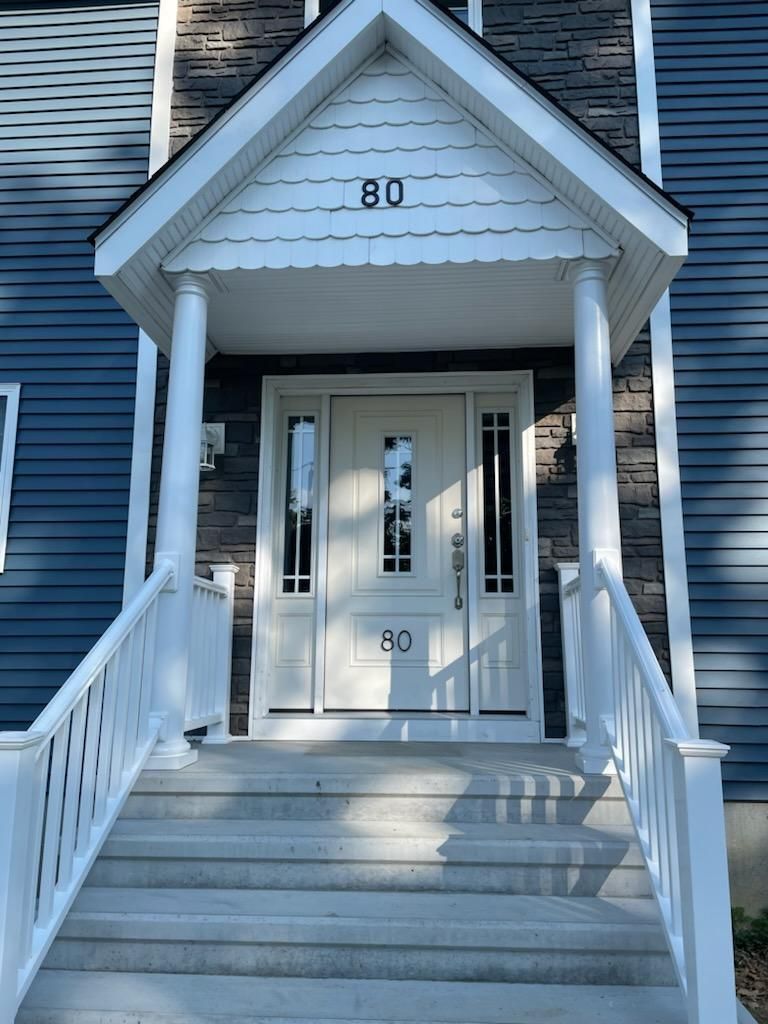 White front door with pillars and steps leading up to entrance of a blue house. Number 80 on door and overhead.