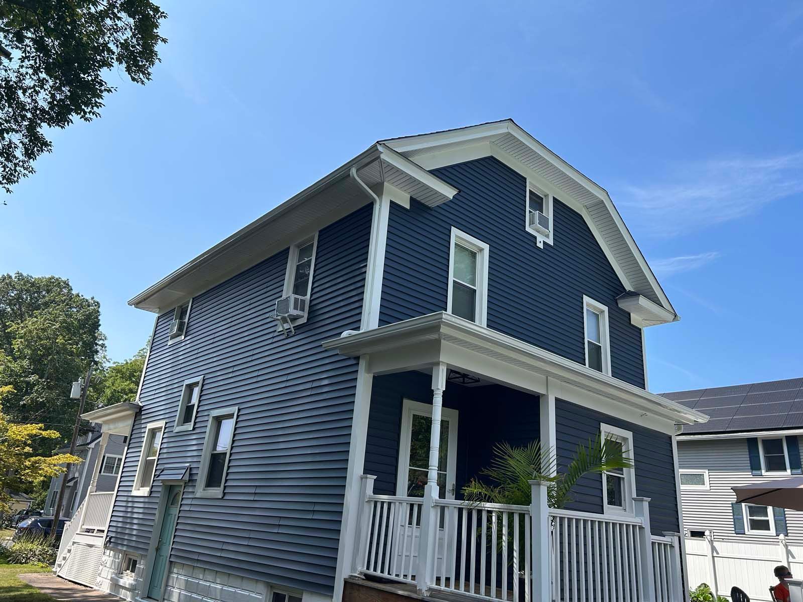 Blue house with white trim against a blue sky. Porch with white railing and windows.