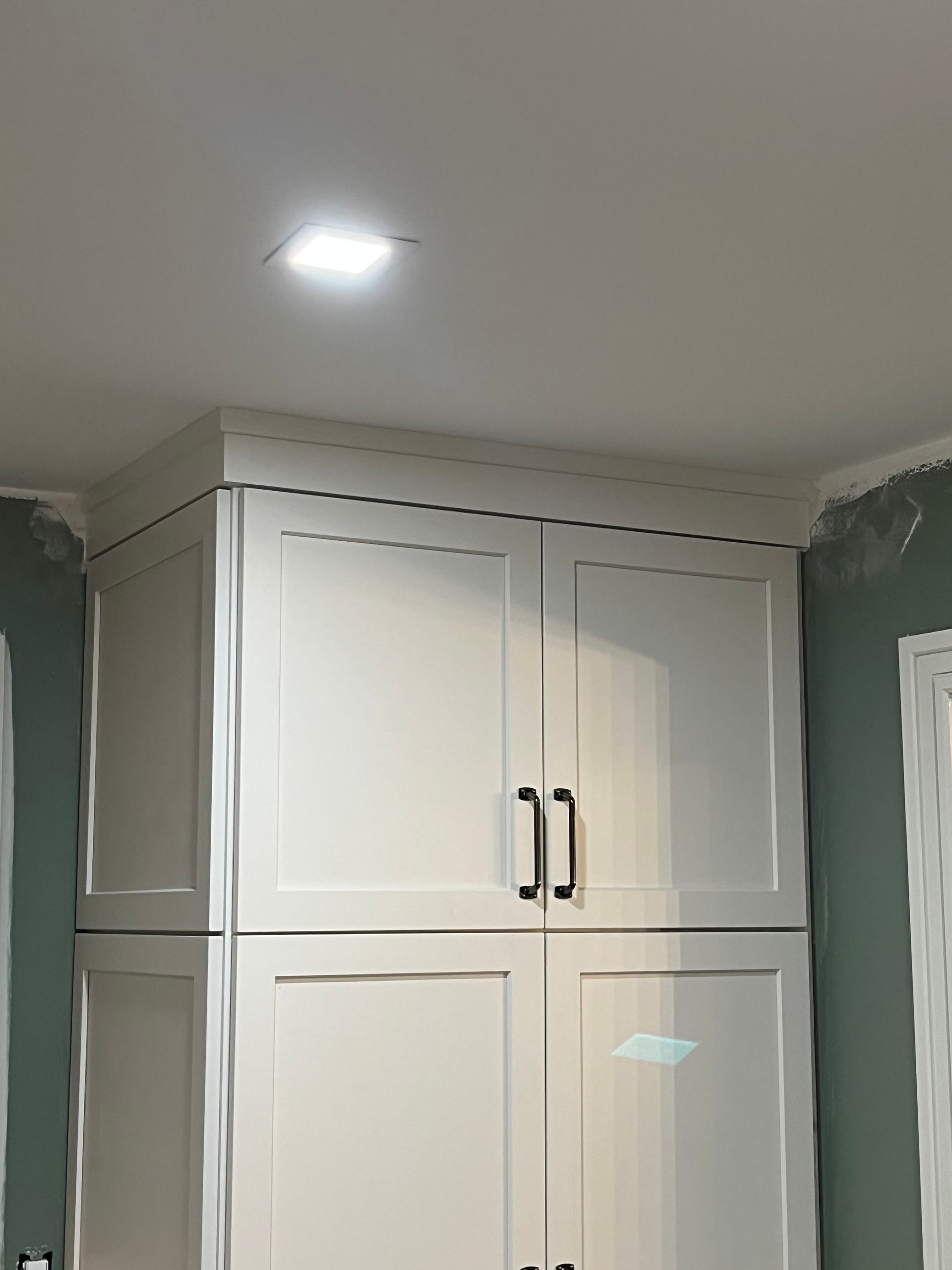 White kitchen cabinets with black handles, a crown molding, and a light in the ceiling.