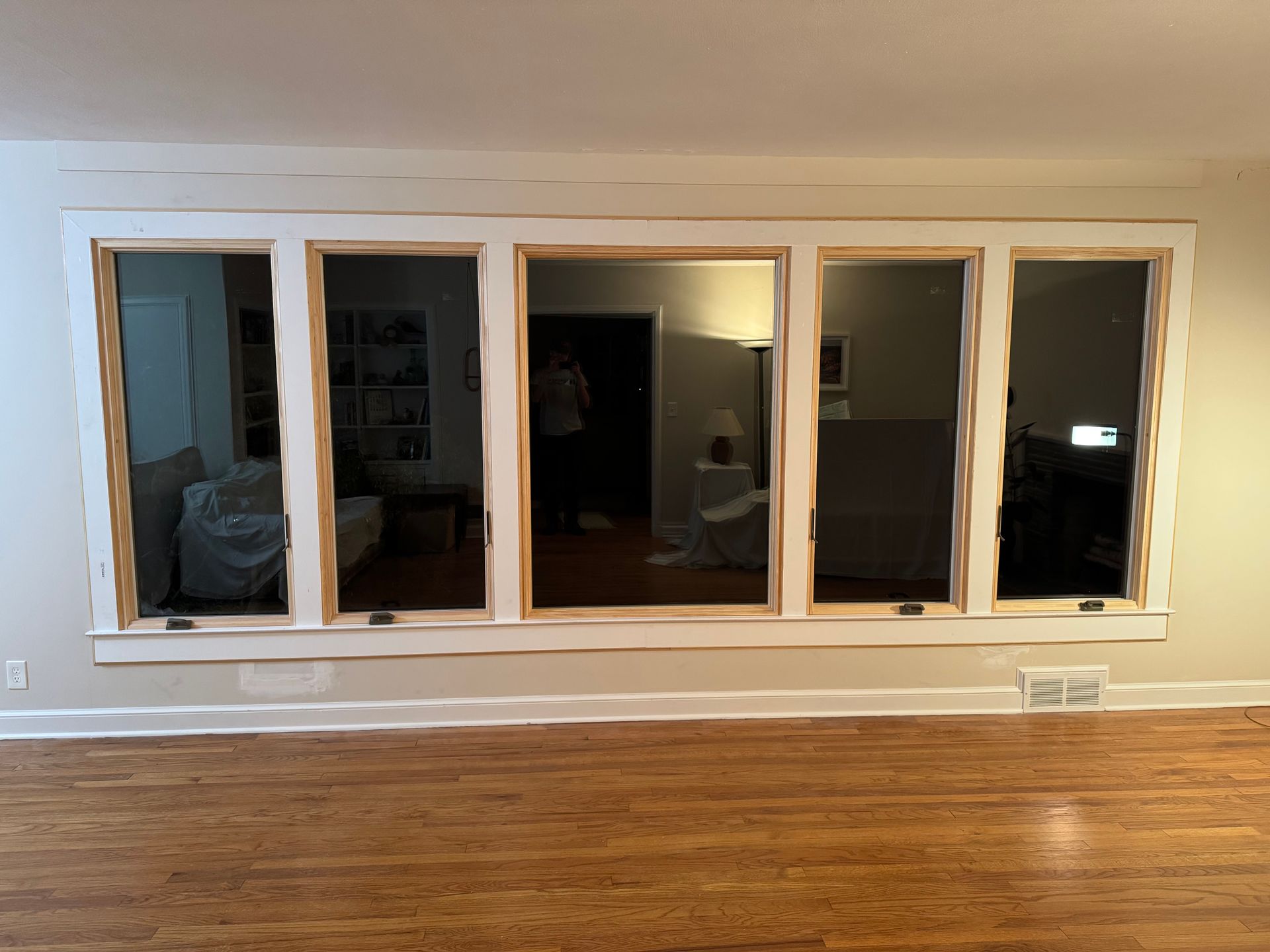 Five rectangular windows set in a white frame, reflecting interior rooms. Wooden floor, beige walls.