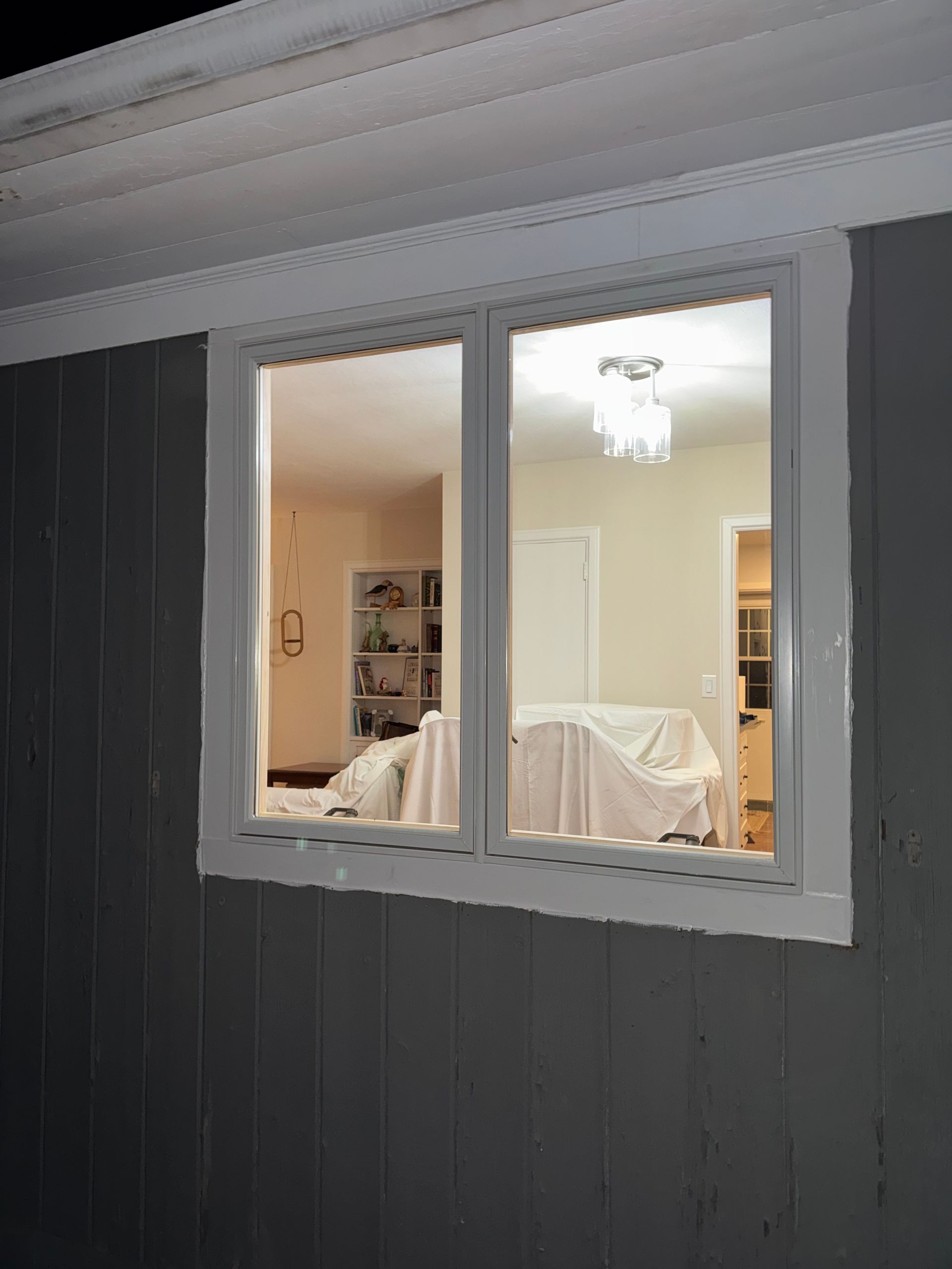 Window showing a view of a lit interior, including a table covered with a sheet and a hanging light fixture.